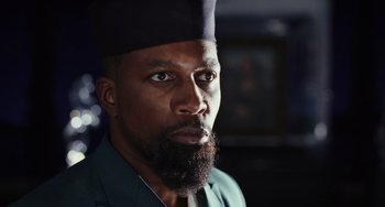 Movie still from “Glass Onion” (2022), directed by Rian Johnson – A person with a beard wearing a hat; Close Up shot, Over the shoulder angle