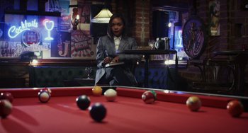 Movie still from “Glass Onion” (2022), directed by Rian Johnson – A woman sitting at a pool table in front of a red pool table; Medium shot, Over the shoulder angle