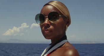 Movie still from “Glass Onion” (2022), directed by Rian Johnson – A woman wearing sunglasses standing in front of a body of water; Close Up shot, Low angle