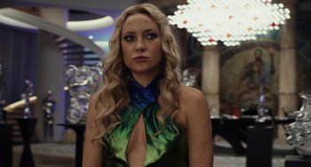 Movie still from “Glass Onion” (2022), directed by Rian Johnson – A woman with long blonde hair wearing a green and blue dress; Close Up shot, Over the shoulder angle