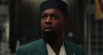 Movie still from “Glass Onion” (2022), directed by Rian Johnson – A man with a beard wearing a green jacket and a black hat; Close Up shot, Low angle