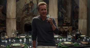 Movie still from “Glass Onion” (2022), directed by Rian Johnson – A man holding a wine glass in front of a dinner table; Medium shot, Over the shoulder angle