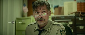 Movie still from “God Is a Bullet” (2023), directed by Nick Cassavetes – A man in a police uniform wearing glasses; Close Up shot, Over the shoulder angle