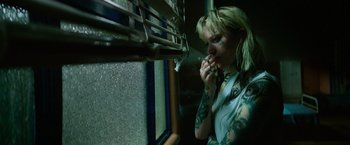 Movie still from “God Is a Bullet” (2023), directed by Nick Cassavetes – A woman with tattoos eating a sandwich in front of a window; Close Up shot, High angle