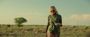 Movie still from “God Is a Bullet” (2023), directed by Nick Cassavetes – A woman with tattoos holding a frisbee in a field; Medium shot, Over the shoulder angle