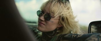 Movie still from “God Is a Bullet” (2023), directed by Nick Cassavetes – A woman with a tattoo on her arm wearing sunglasses; Close Up shot, Low angle