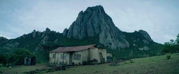 Movie still from “God Is a Bullet” (2023), directed by Nick Cassavetes – An old house in the middle of a field with a mountain in the background; Extreme Wide shot, Low angle