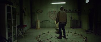 Movie still from “God Is a Bullet” (2023), directed by Nick Cassavetes – A man standing in front of a circle of nails in a room; Wide shot, High angle