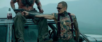 Movie still from “God Is a Bullet” (2023), directed by Nick Cassavetes – A man sitting on the hood of a car with another man standing next to him; Medium shot, Low angle