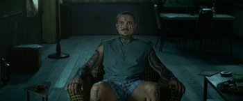 Movie still from “God Is a Bullet” (2023), directed by Nick Cassavetes – A man sitting in a chair with lots of tattoos on his arms and face; Medium shot, High angle