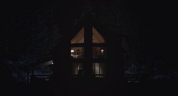 Movie still from “God's Country” (2022), directed by Julian Higgins – A person standing in front of a window at night; Extreme Wide shot, Low angle