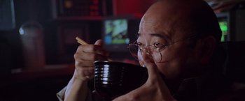 Movie still from “Godzilla” (1998), directed by Roland Emmerich – An older man holding a bowl of food and chopsticks in front of his face; Close Up shot, Low angle