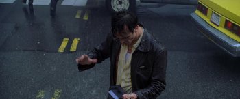 Movie still from “Godzilla” (1998), directed by Roland Emmerich – A man holding a cell phone while standing in the rain; Medium shot, High angle