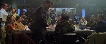 Movie still from “Godzilla” (1998), directed by Roland Emmerich – A group of men sitting at a table in a room; Medium shot, Over the shoulder angle