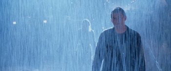 Movie still from “Godzilla” (1998), directed by Roland Emmerich – A man standing in the rain with a woman standing in the background; Medium shot, Low angle