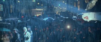 Movie still from “Godzilla” (1998), directed by Roland Emmerich – A group of people standing in the rain holding umbrellas; Wide shot, Over the shoulder angle