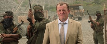 Movie still from “Godzilla” (2014), directed by Gareth Edwards – A man in a suit and tie standing next to a man in a suit and tie; Medium shot, Over the shoulder angle