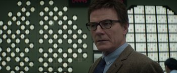 Movie still from “Godzilla” (2014), directed by Gareth Edwards – A man wearing glasses and a suit in front of a wall of clocks; Close Up shot, Over the shoulder angle