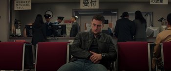Movie still from “Godzilla” (2014), directed by Gareth Edwards – A man sitting on a chair in front of an airport terminal; Medium shot, Low angle