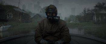 Movie still from “Godzilla” (2014), directed by Gareth Edwards – A man wearing a gas mask sitting in front of a lake; Medium shot, Low angle