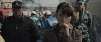 Movie still from “Godzilla” (2014), directed by Gareth Edwards – A woman standing in front of a group of people; Close Up shot, Over the shoulder angle