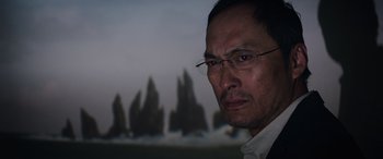 Movie still from “Godzilla” (2014), directed by Gareth Edwards – A person wearing glasses and a white shirt; Close Up shot, Over the shoulder angle
