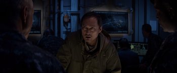 Movie still from “Godzilla” (2014), directed by Gareth Edwards – A man in a brown jacket sitting in front of a television; Close Up shot, Low angle
