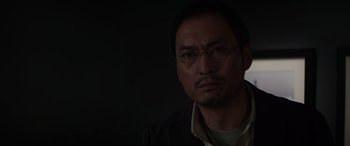 Movie still from “Godzilla” (2014), directed by Gareth Edwards – A person wearing glasses and a jacket; Close Up shot, Low angle