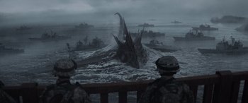 Movie still from “Godzilla” (2014), directed by Gareth Edwards – Two men in camouflage standing in front of an ocean with ships; Extreme Wide shot, High angle