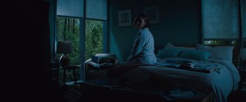 Movie still from “Godzilla: King of the Monsters” (2019), directed by Michael Dougherty – A woman sitting on a bed in front of a window; Wide shot, Low angle