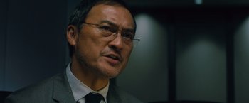 Movie still from “Godzilla: King of the Monsters” (2019), directed by Michael Dougherty – A man in a suit and tie wearing glasses; Close Up shot, Low angle