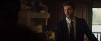 Movie still from “Godzilla: King of the Monsters” (2019), directed by Michael Dougherty – A man wearing a suit and tie in front of a fire place; Medium shot, Over the shoulder angle