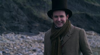 Movie still from “Ammonite” (2020), directed by Francis Lee – A man wearing a top hat and a scarf; Close Up shot, Over the shoulder angle