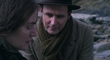 Movie still from “Ammonite” (2020), directed by Francis Lee – A man wearing a hat and a brown scarf; Close Up shot, Over the shoulder angle
