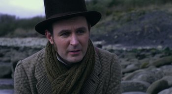 Movie still from “Ammonite” (2020), directed by Francis Lee – A man wearing a hat and a scarf; Close Up shot, Over the shoulder angle