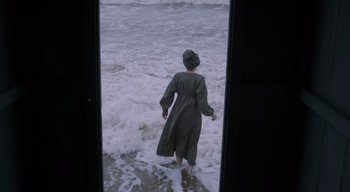 Movie still from “Ammonite” (2020), directed by Francis Lee – A woman in a robe standing in the water; Wide shot, High angle