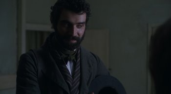 Movie still from “Ammonite” (2020), directed by Francis Lee – A man in a suit and tie standing next to a wall; Close Up shot, Over the shoulder angle