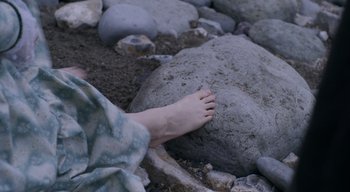 Movie still from “Ammonite” (2020), directed by Francis Lee – A person's bare foot on the ground next to rocks; Extreme Close Up shot, High angle