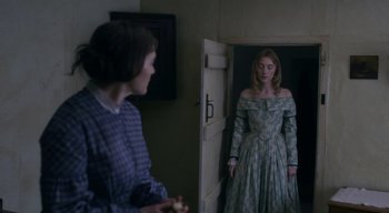 Movie still from “Ammonite” (2020), directed by Francis Lee – A woman in a dress standing in front of another woman in a dress; Medium shot, Over the shoulder angle