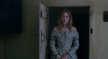 Movie still from “Ammonite” (2020), directed by Francis Lee – A woman in a dress standing in front of an open door; Medium shot, Over the shoulder angle