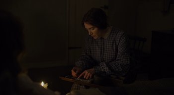 Movie still from “Ammonite” (2020), directed by Francis Lee – A person sitting in a chair using a computer; Medium shot, High angle