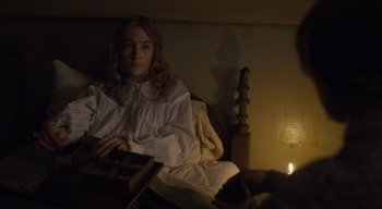Movie still from “Ammonite” (2020), directed by Francis Lee – A woman sitting on a bed with a candle in a room; Medium shot, High angle