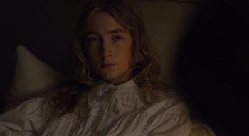 Movie still from “Ammonite” (2020), directed by Francis Lee – A woman in a white shirt is sitting in a dark room; Close Up shot, High angle