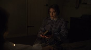Movie still from “Ammonite” (2020), directed by Francis Lee – A woman sitting on the floor holding a book; Medium shot, High angle