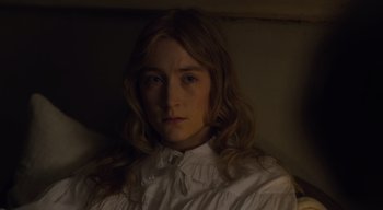 Movie still from “Ammonite” (2020), directed by Francis Lee – A woman in a white shirt is sitting in a dark room; Close Up shot, High angle