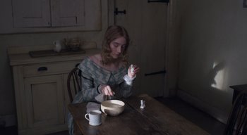 Movie still from “Ammonite” (2020), directed by Francis Lee – A woman sitting at a wooden table with a bowl of food; Medium shot, High angle