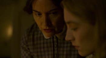 Movie still from “Ammonite” (2020), directed by Francis Lee – A man and a woman looking at each other in a dimly - lit room; Close Up shot, Over the shoulder angle