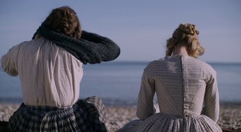 Movie still from “Ammonite” (2020), directed by Francis Lee – Two women sitting on the beach looking out at the ocean; Medium shot, Over the shoulder angle