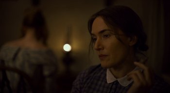 Movie still from “Ammonite” (2020), directed by Francis Lee – A woman sitting in front of a candle light; Close Up shot, Over the shoulder angle