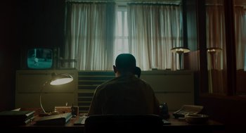 Movie still from “Golda” (2023), directed by Guy Nattiv – A man sitting at a desk in front of a window; Medium shot, Low angle